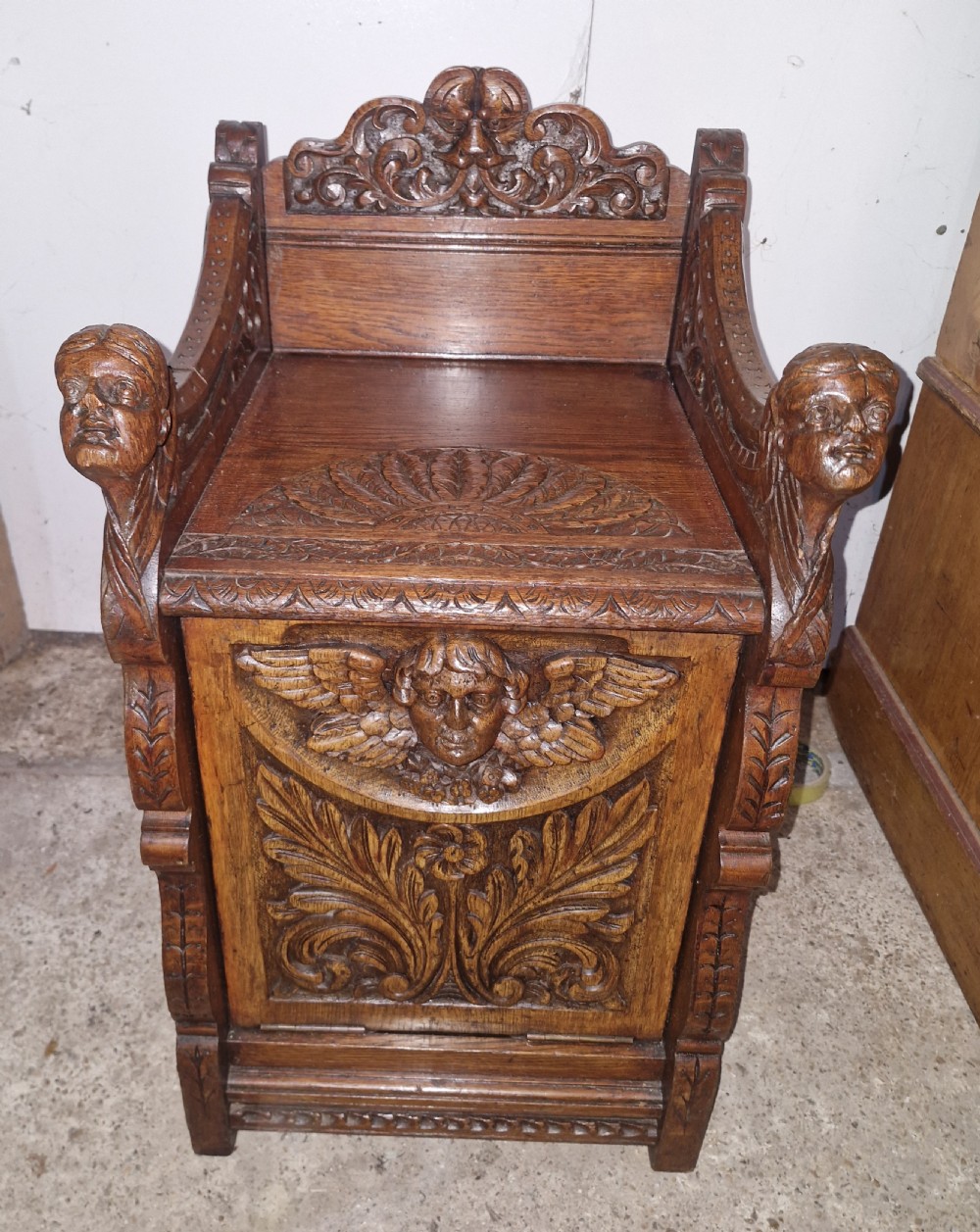 A late Victorian dark oak drop-front cabinet featuring detailed relief carvings of winged cherubs, mascarons, and leaf motifs. View VII