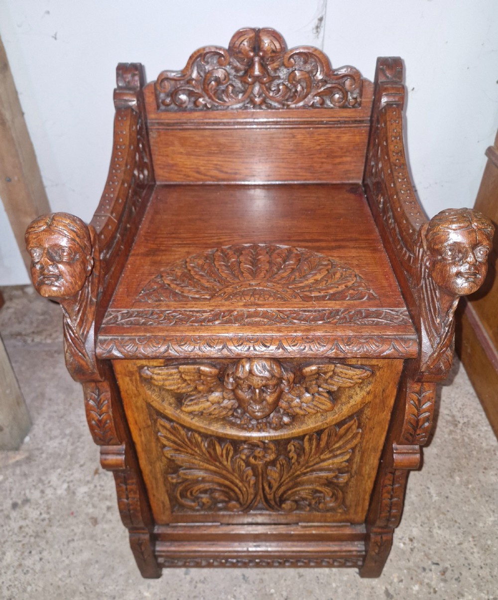 A late Victorian dark oak drop-front cabinet featuring detailed relief carvings of winged cherubs, mascarons, and leaf motifs. View IX