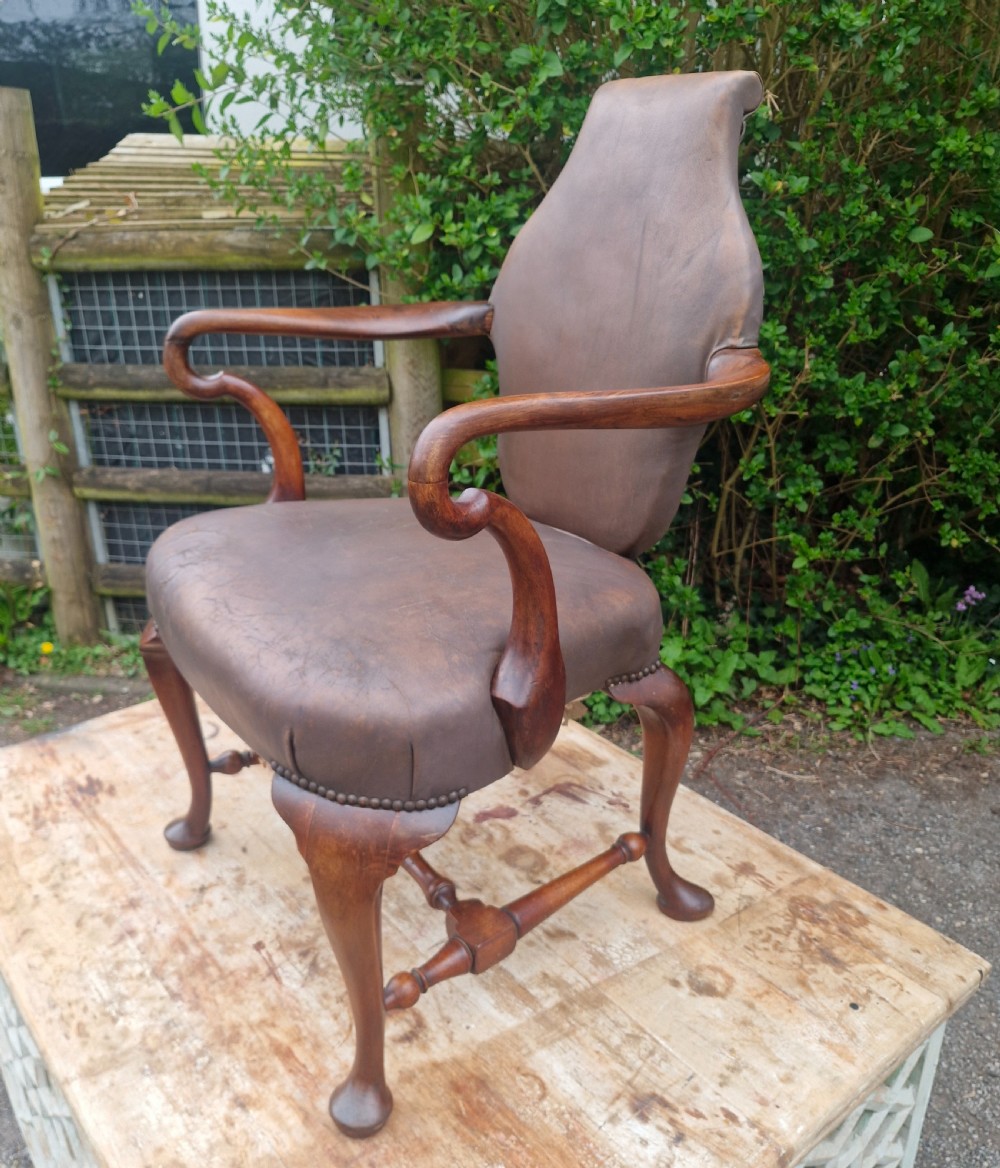 A Queen Anne style desk armchair featuring dark brown leather upholstery, scroll arms, and cabriole legs with turned stretchers.
