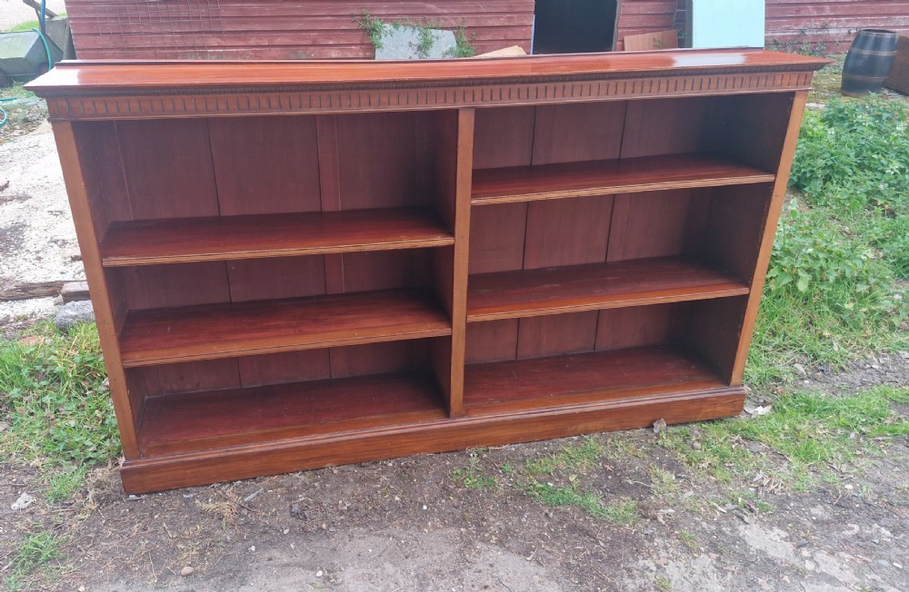 A wide Edwardian mahogany low open-front bookcase with two central bays, adjustable internal shelves, and dentil moulding along the top edge. View V