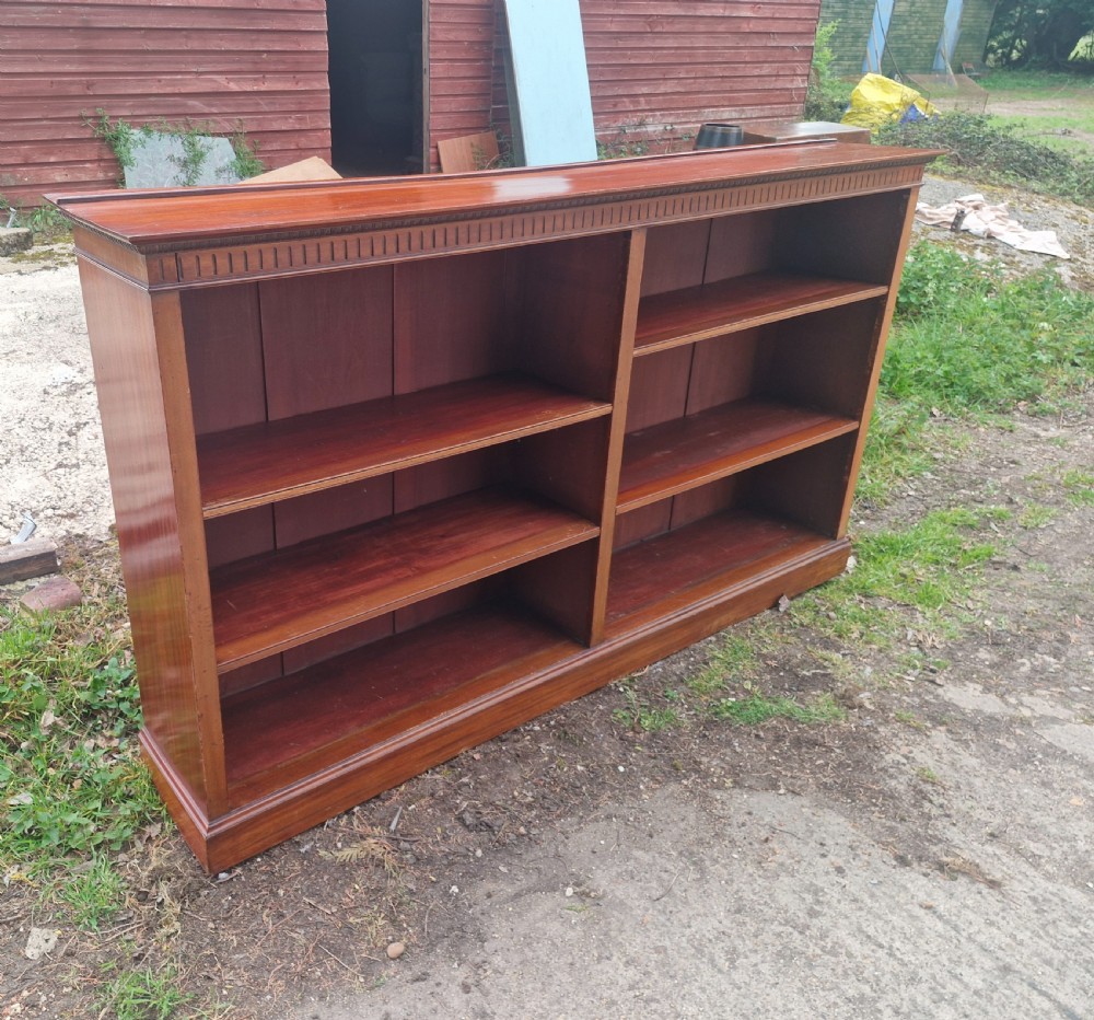 A wide Edwardian mahogany low open-front bookcase with two central bays, adjustable internal shelves, and dentil moulding along the top edge. View VI