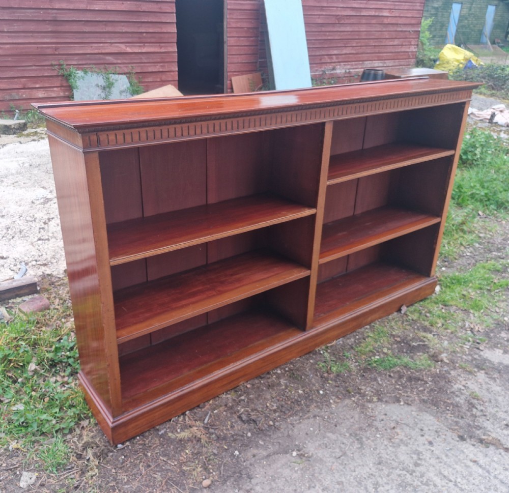 A wide Edwardian mahogany low open-front bookcase with two central bays, adjustable internal shelves, and dentil moulding along the top edge. View VII