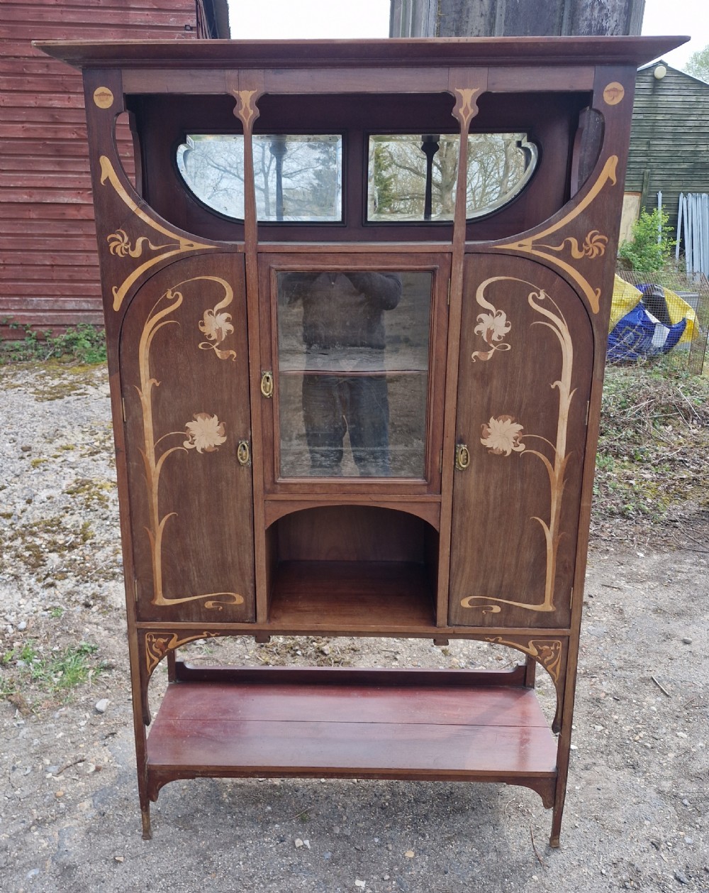 An Art Nouveau mahogany display cabinet with floral marquetry inlay, a central glazed door, an upper mirror section, and an open lower shelf. View IV