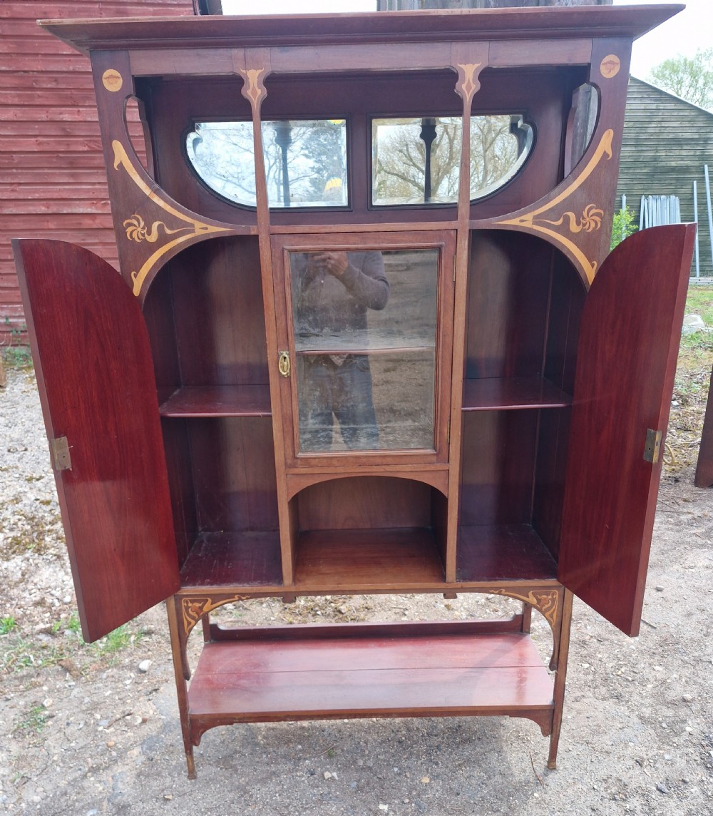 An Art Nouveau mahogany display cabinet with floral marquetry inlay, a central glazed door, an upper mirror section, and an open lower shelf. View VI