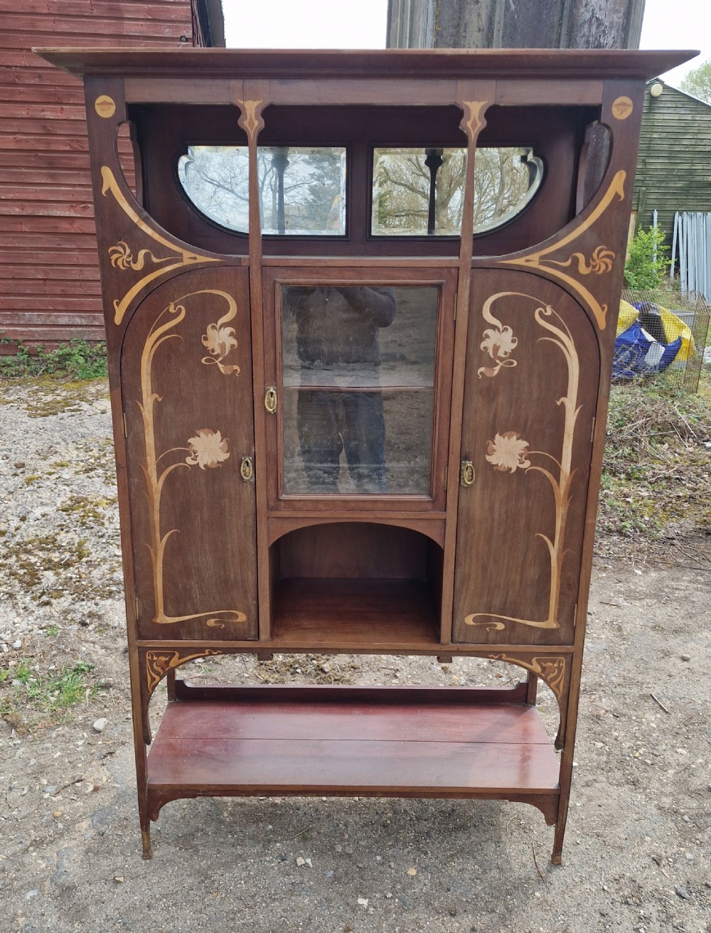 An Art Nouveau mahogany display cabinet with floral marquetry inlay, a central glazed door, an upper mirror section, and an open lower shelf. View IX