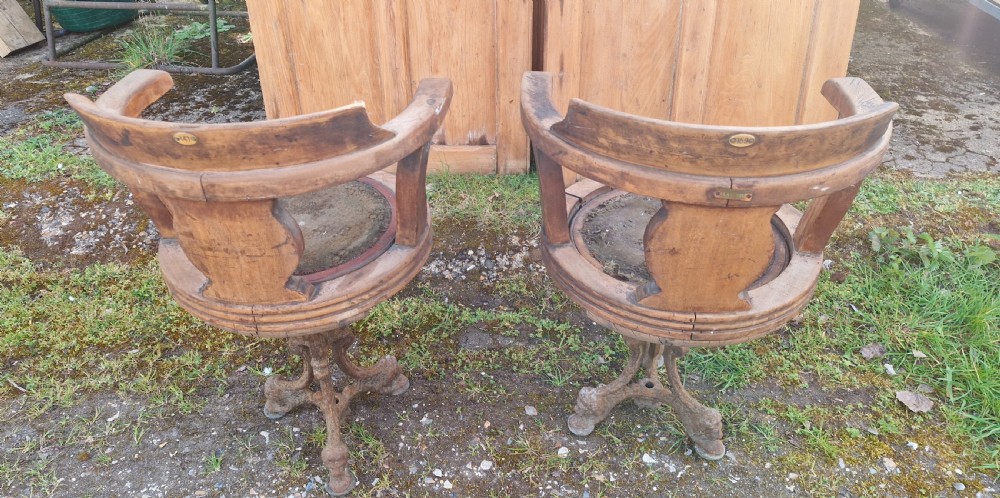 A pair of antique wooden ocean liner revolving armchairs featuring carved monograms on the back splats and cast iron swivel bases. View VII