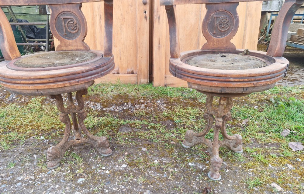 A pair of antique wooden ocean liner revolving armchairs featuring carved monograms on the back splats and cast iron swivel bases. View IX