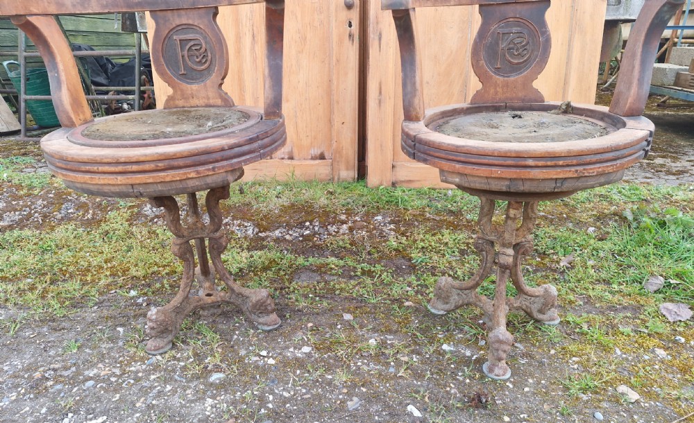A pair of antique wooden ocean liner revolving armchairs featuring carved monograms on the back splats and cast iron swivel bases. View X