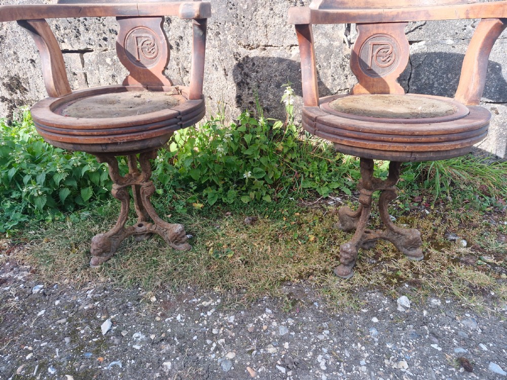 A pair of antique wooden ocean liner revolving armchairs featuring carved monograms on the back splats and cast iron swivel bases. View XII