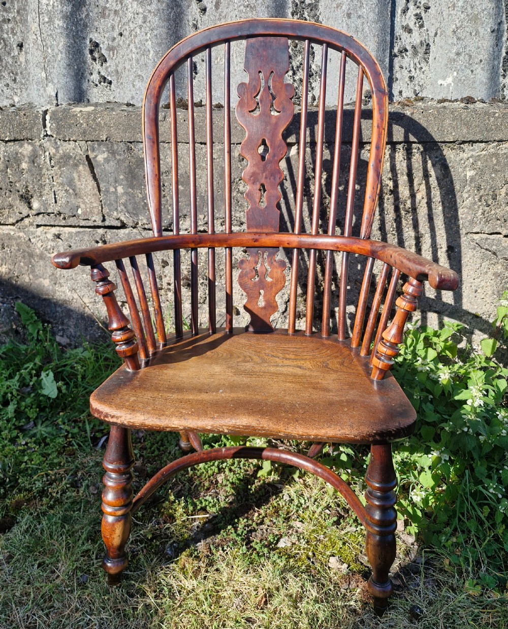 A mid-19th-century yewwood Windsor armchair featuring a hoop back, pierced central splat, turned legs, and a saddle-shaped wooden seat.