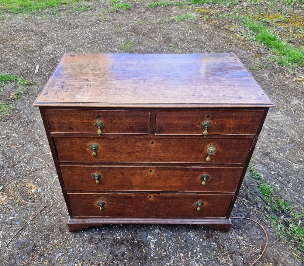 An early nineteenth-century oak chest of drawers featuring two short drawers above three long drawers with brass drop handles and a moulded top edge.