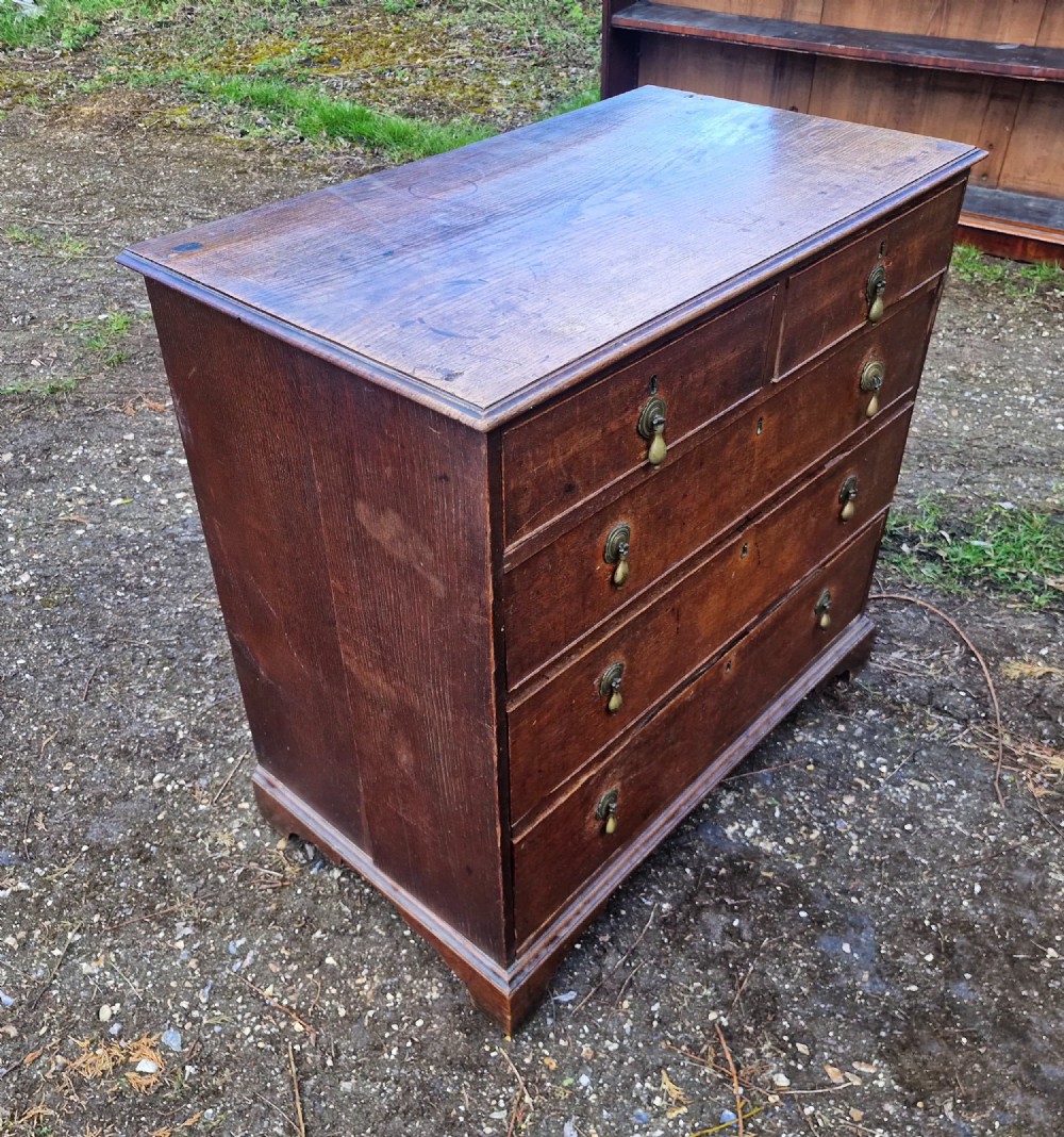 An early nineteenth-century oak chest of drawers featuring two short drawers above three long drawers with brass drop handles and a moulded top edge. View II
