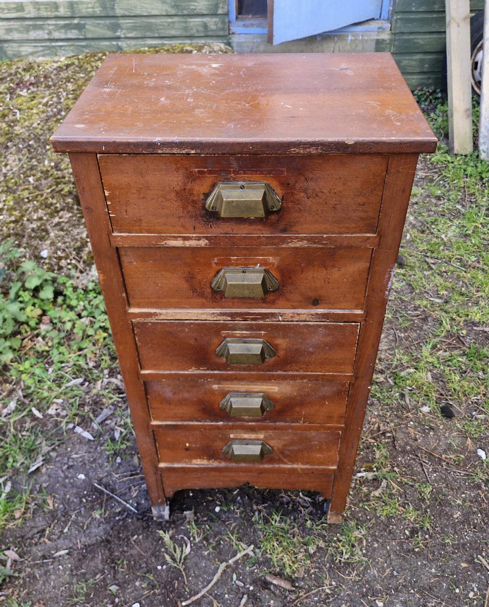 A medium brown vintage wooden five-drawer vertical office cabinet with brass cup handles.
