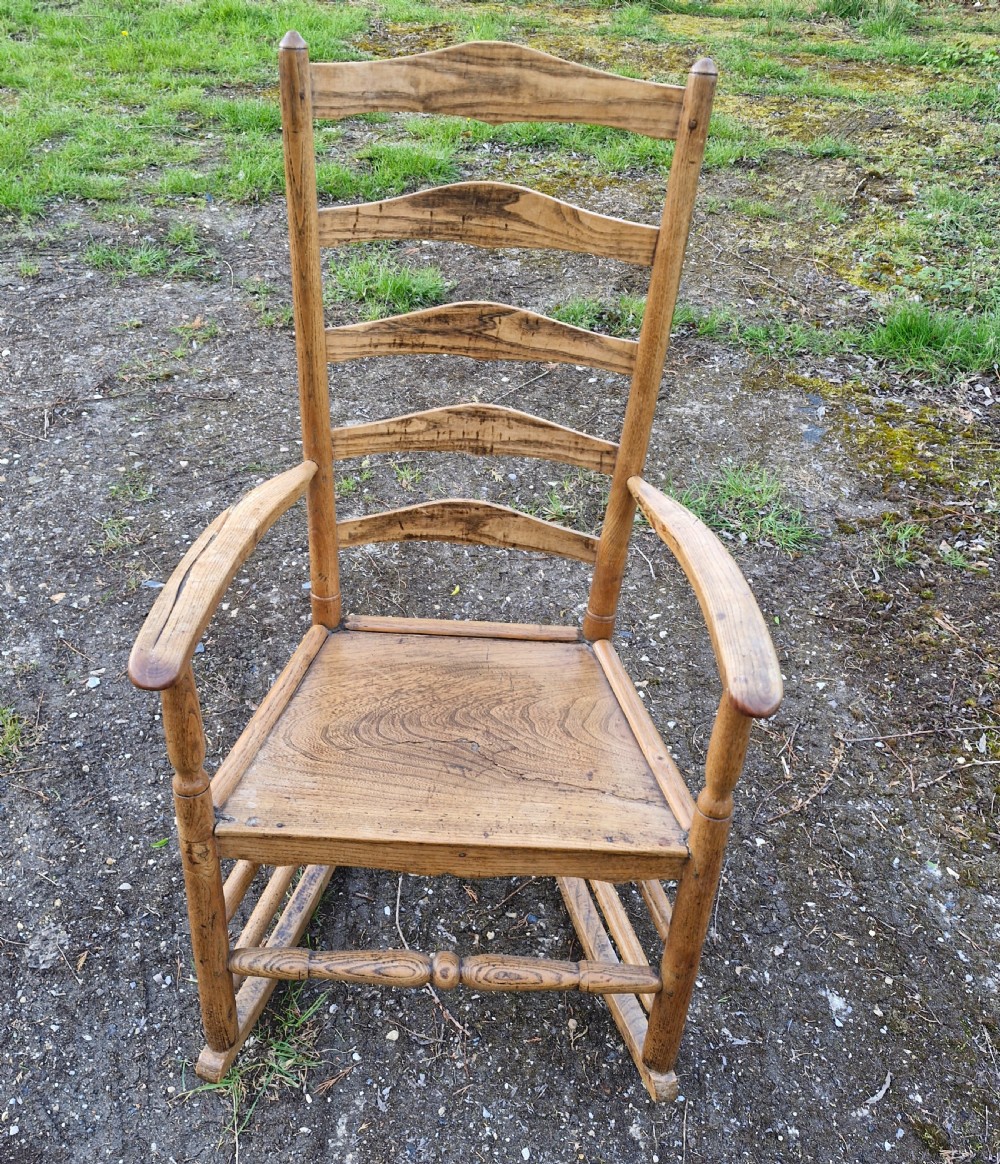 An early 19th century wooden ladderback rocking armchair with curved armrests, turned stretchers, and a patterned cushion. View II