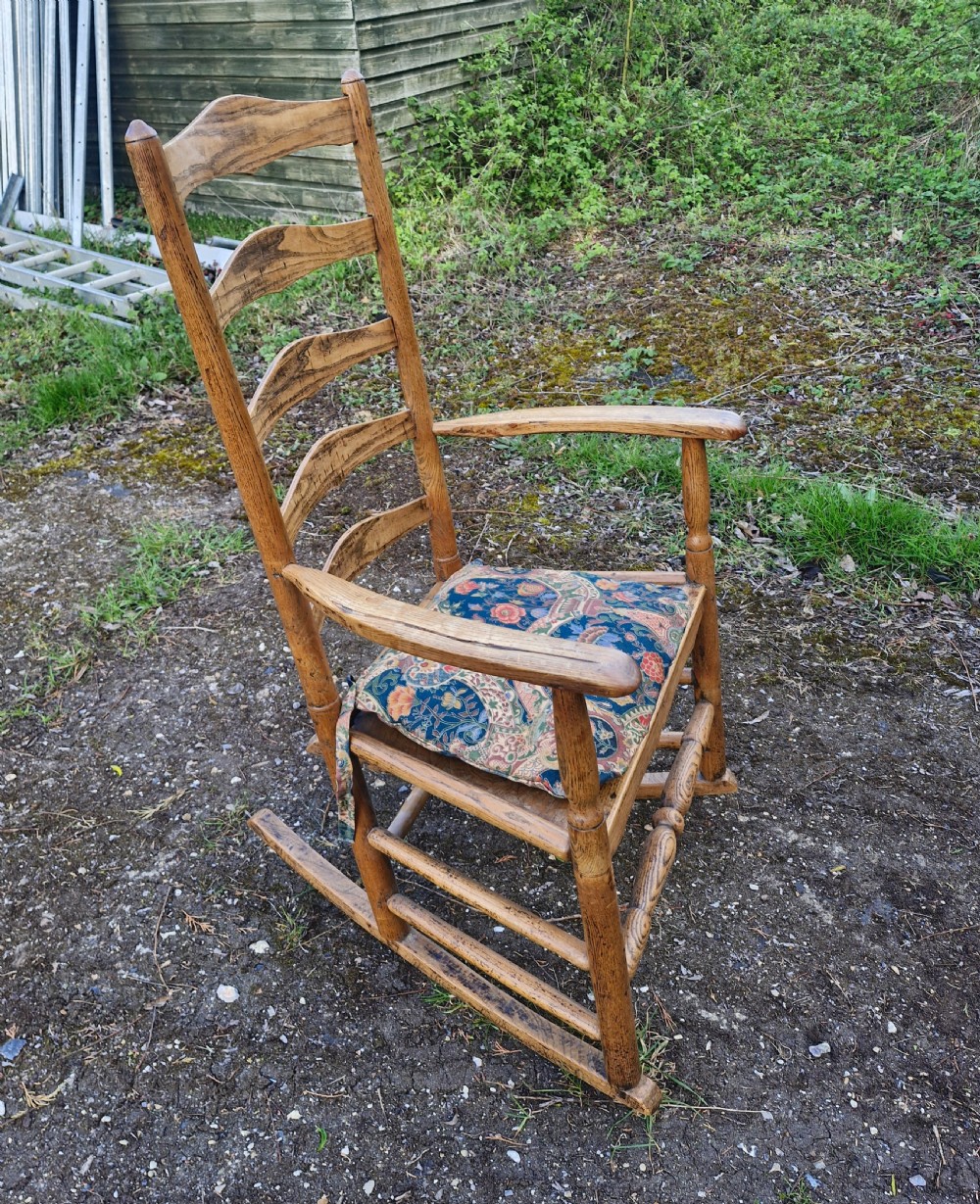 An early 19th century wooden ladderback rocking armchair with curved armrests, turned stretchers, and a patterned cushion. View IV