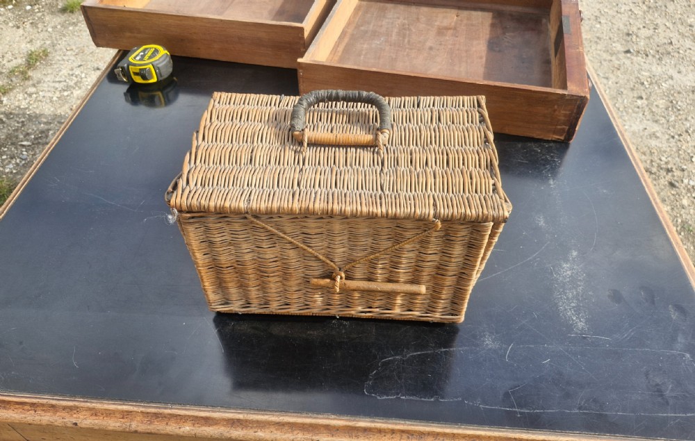 An antique woven wicker travelling hamper displayed open alongside white porcelain teacups, saucers, spoons, a metal spirit kettle, and a glass bottle. View VIII
