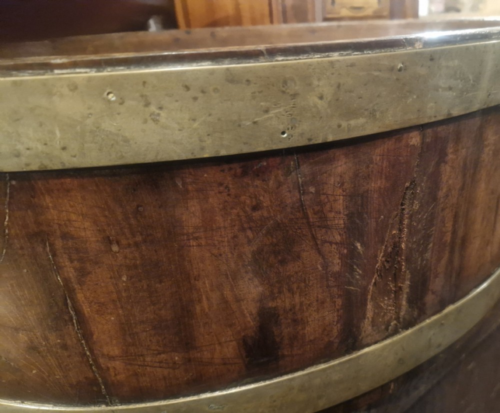 An oval late Georgian mahogany wine cooler with dual brass bands, brass lion mask ring handles, resting on a four-legged stand. View X