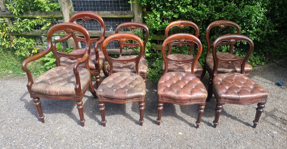 A set of eight Victorian mahogany dining chairs featuring curved balloon backs, turned front legs, and button-tufted brown leather seats. View II