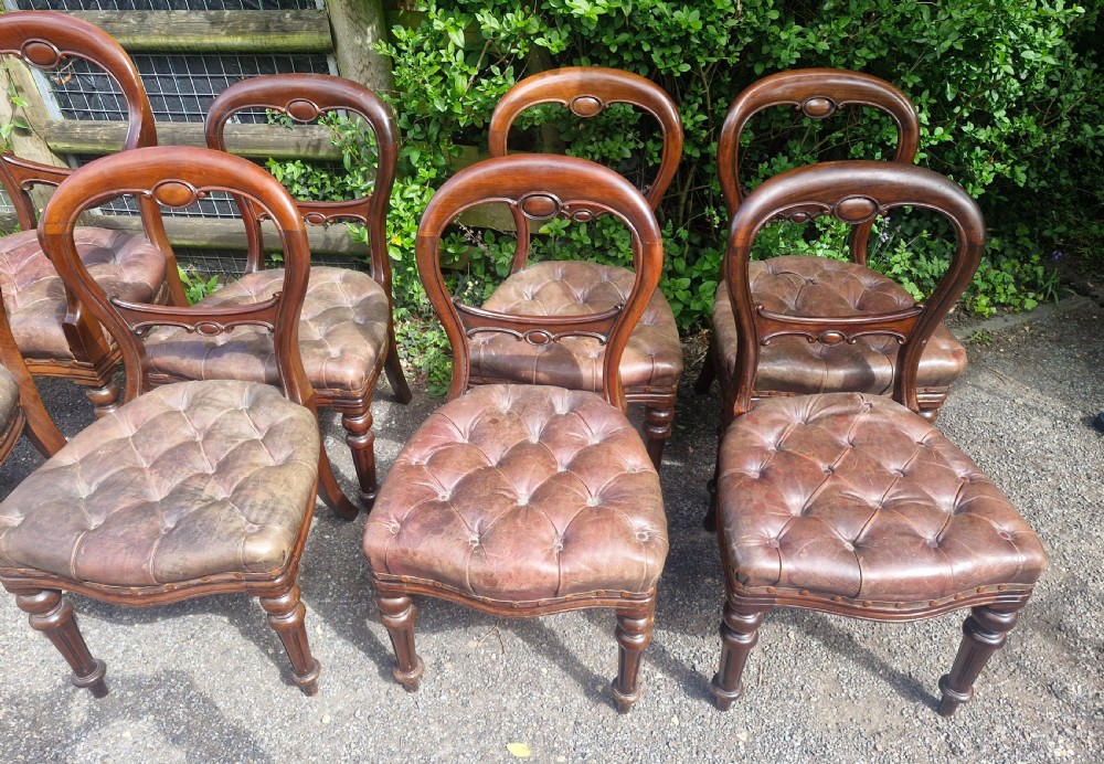 A set of eight Victorian mahogany dining chairs featuring curved balloon backs, turned front legs, and button-tufted brown leather seats. View IV