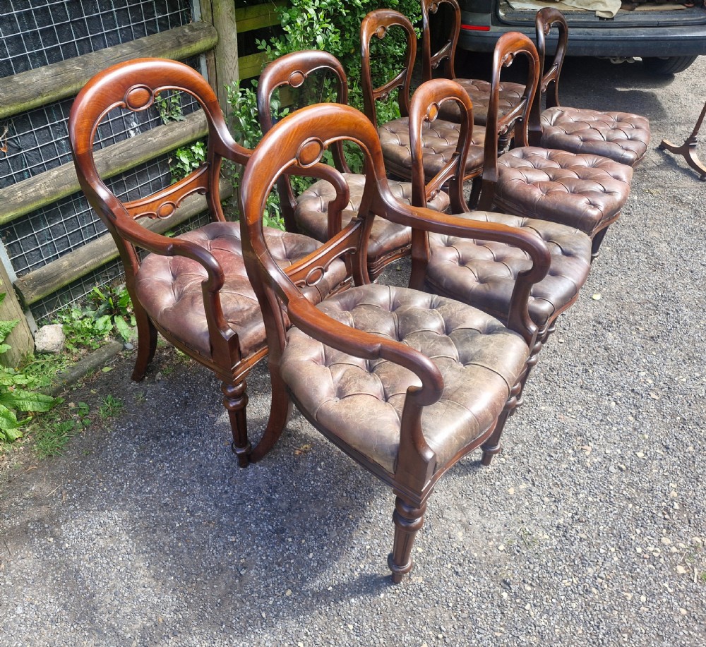 A set of eight Victorian mahogany dining chairs featuring curved balloon backs, turned front legs, and button-tufted brown leather seats. View VI