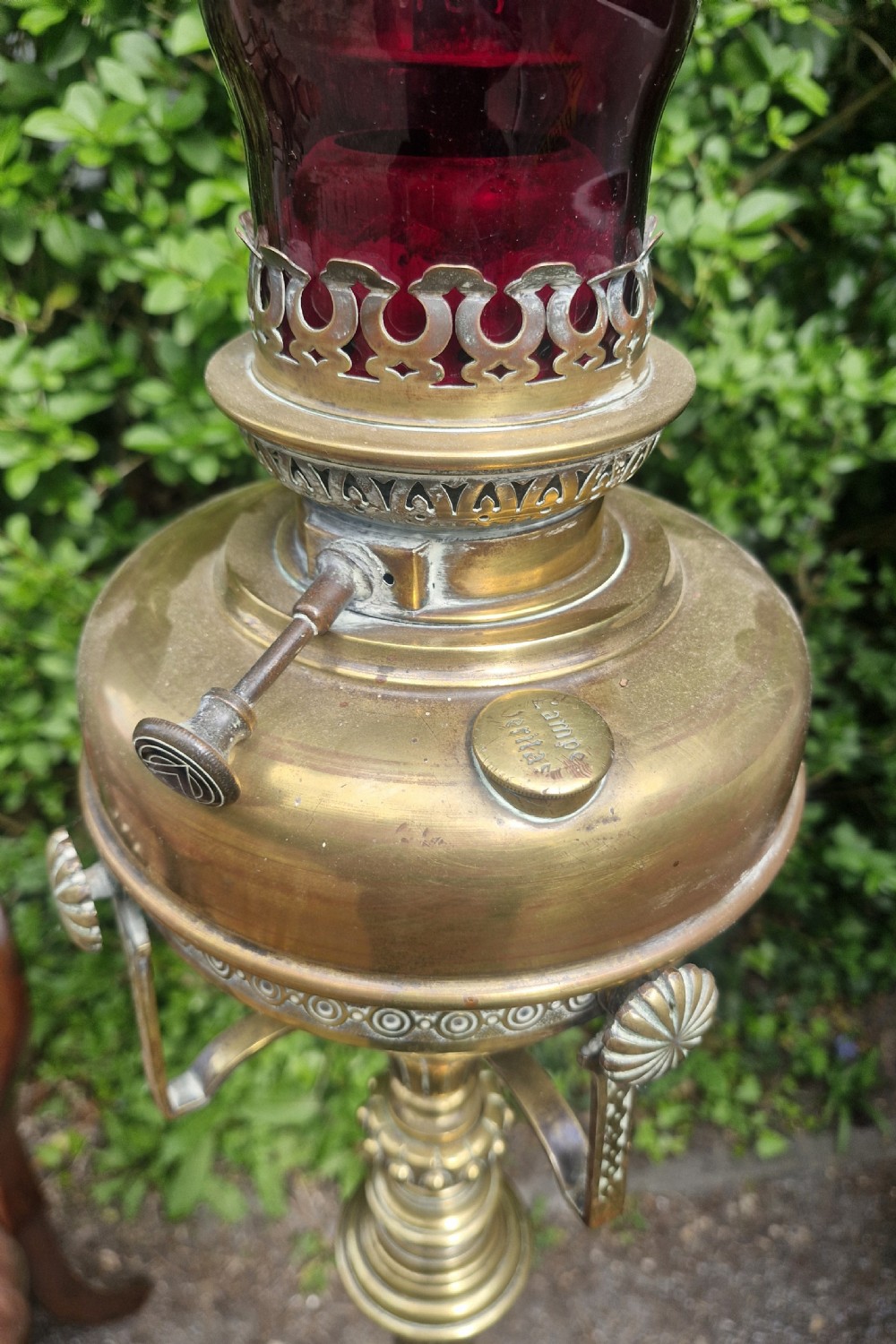 A tall Victorian brass floor lamp featuring a fluted column, gadrooned base with paw feet, and a ruby red glass chimney. View V