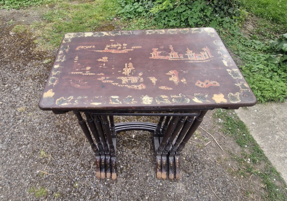 A set of four dark brown lacquered nesting tables decorated with hand-painted gilt chinoiserie landscape scenes and slender turned legs.
