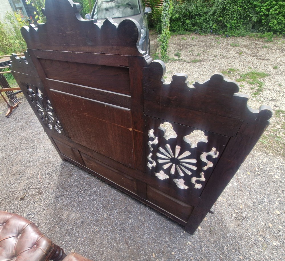 A late nineteenth-century dark carved oak hall bench featuring relief narrative carving, mask pediment, scroll arms, and a hinged seat. View V