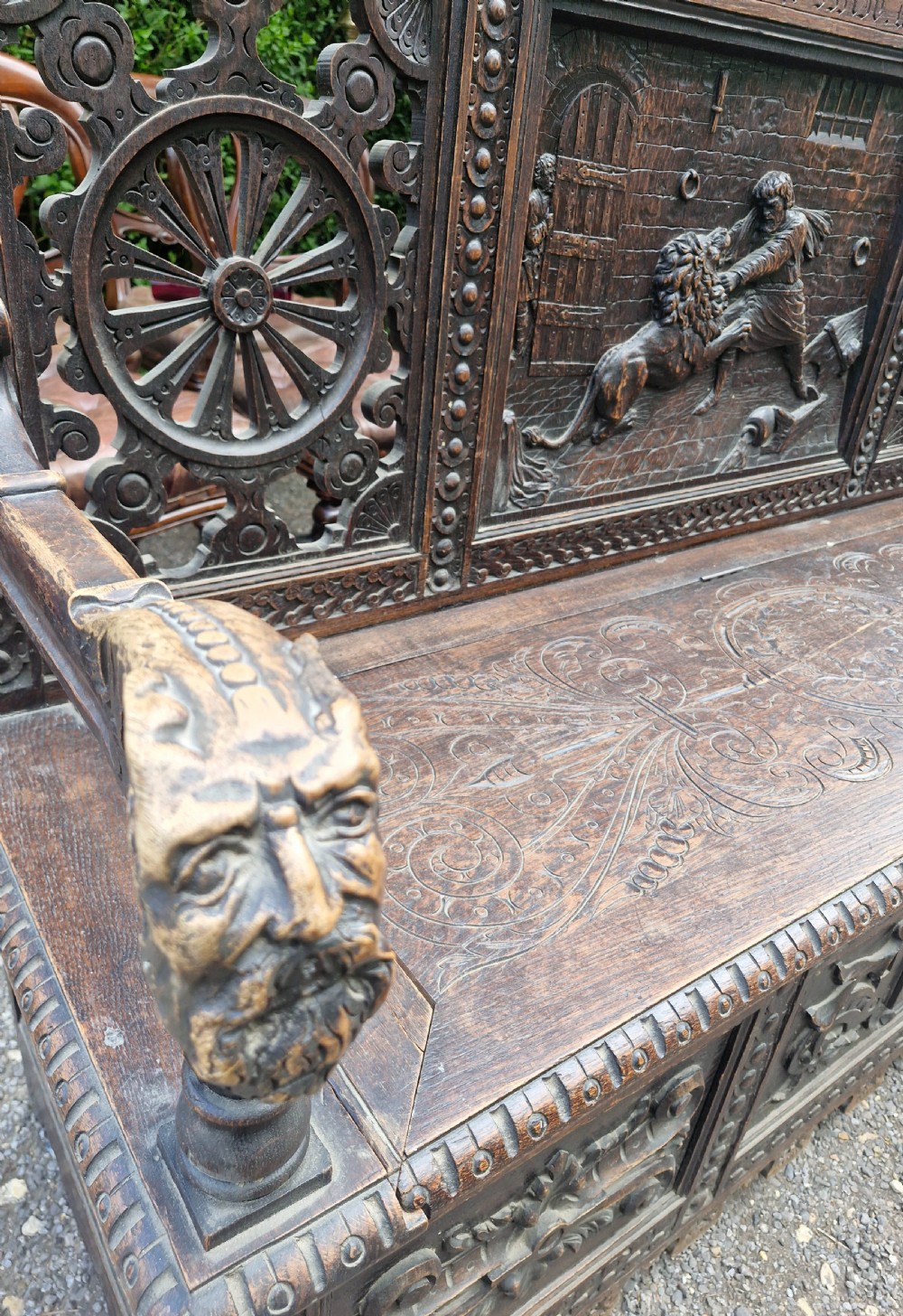 A late nineteenth-century dark carved oak hall bench featuring relief narrative carving, mask pediment, scroll arms, and a hinged seat. View XIV