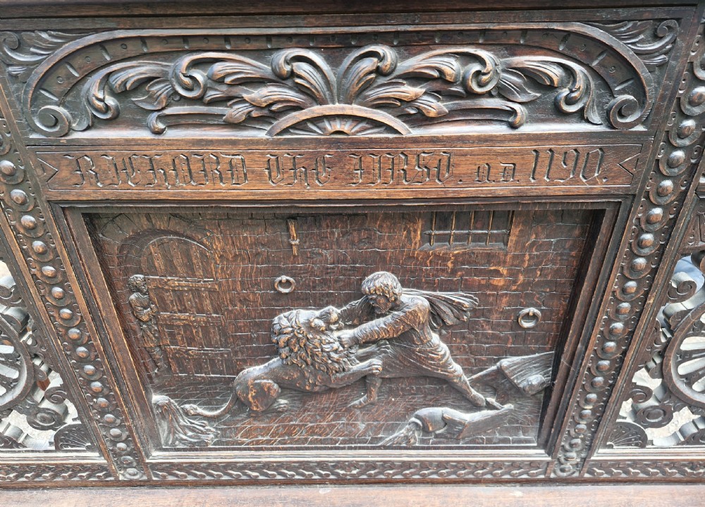 A late nineteenth-century dark carved oak hall bench featuring relief narrative carving, mask pediment, scroll arms, and a hinged seat. View XVI