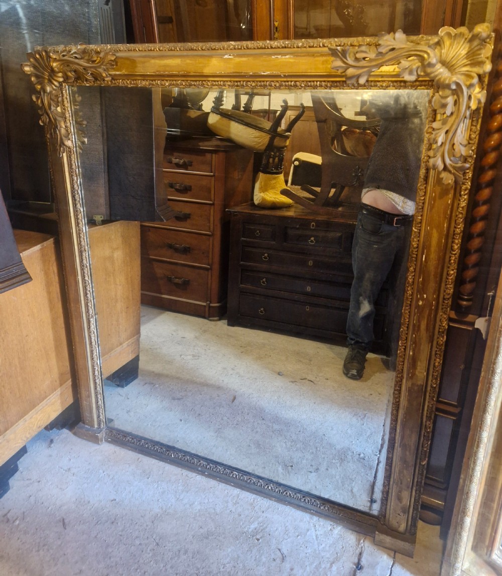 A large rectangular 19th-century overmantel mirror featuring a gilded wood frame with carved acanthus leaves at the top corners and bead moulding along the inner border.