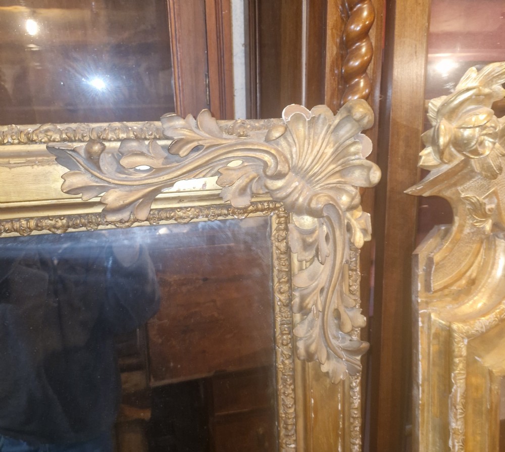 A large rectangular 19th-century overmantel mirror featuring a gilded wood frame with carved acanthus leaves at the top corners and bead moulding along the inner border. View XI