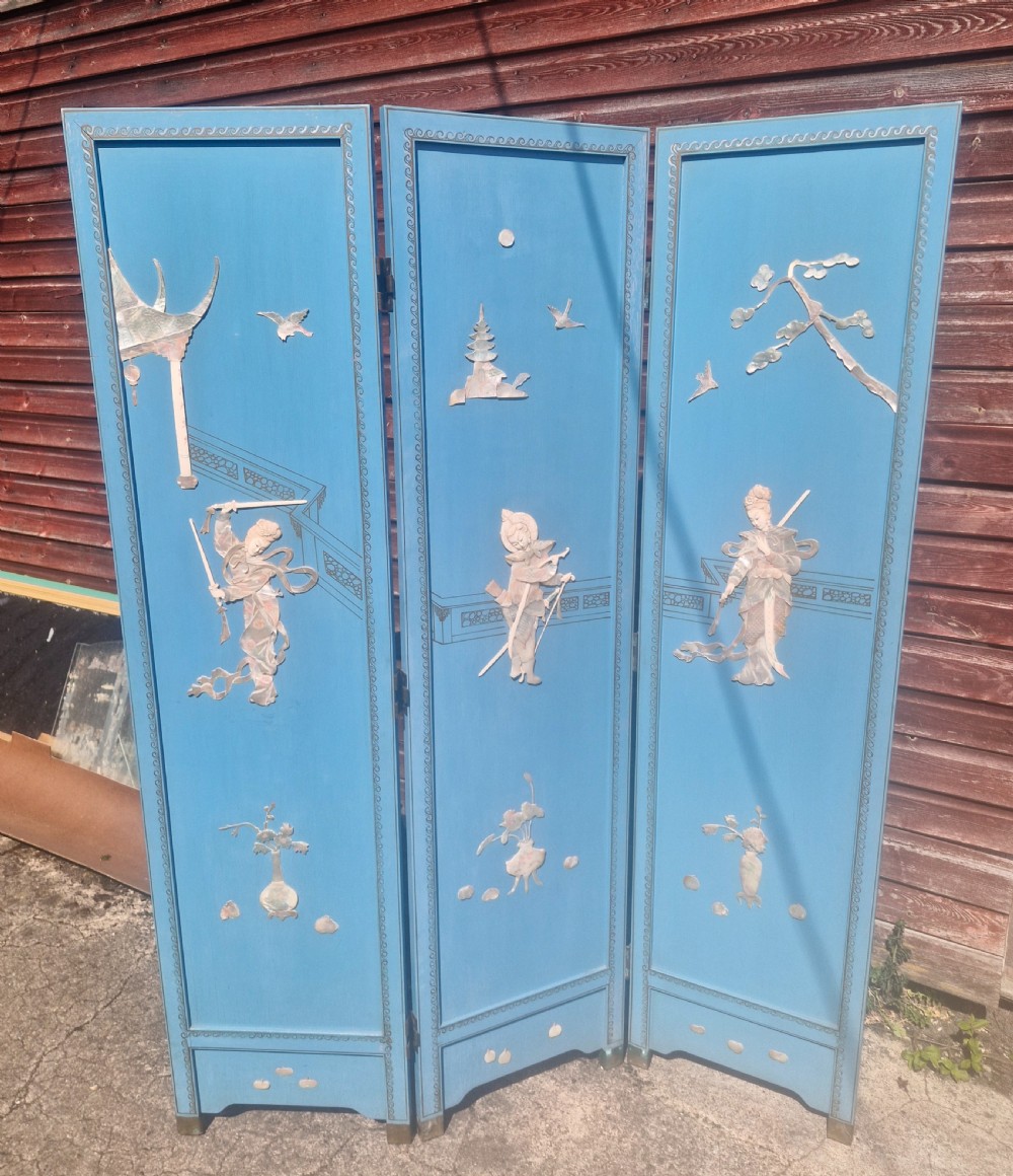 A painted blue three-panel folding screen decorated with mother-of-pearl inlaid figures, pagodas, birds, and botanical motifs.