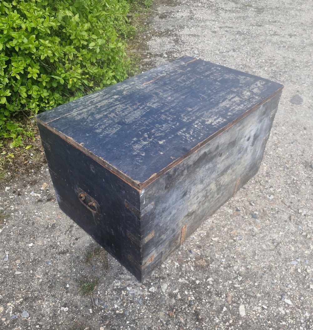 A rectangular antique dark-painted wooden campaign trunk with iron corner brackets and side carrying handles.