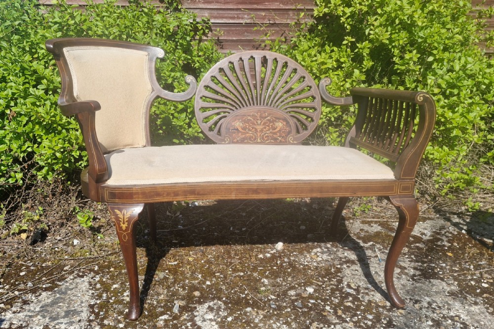 An Edwardian inlaid mahogany window seat with cream upholstery, a central carved fan splat, and scrolled arms.