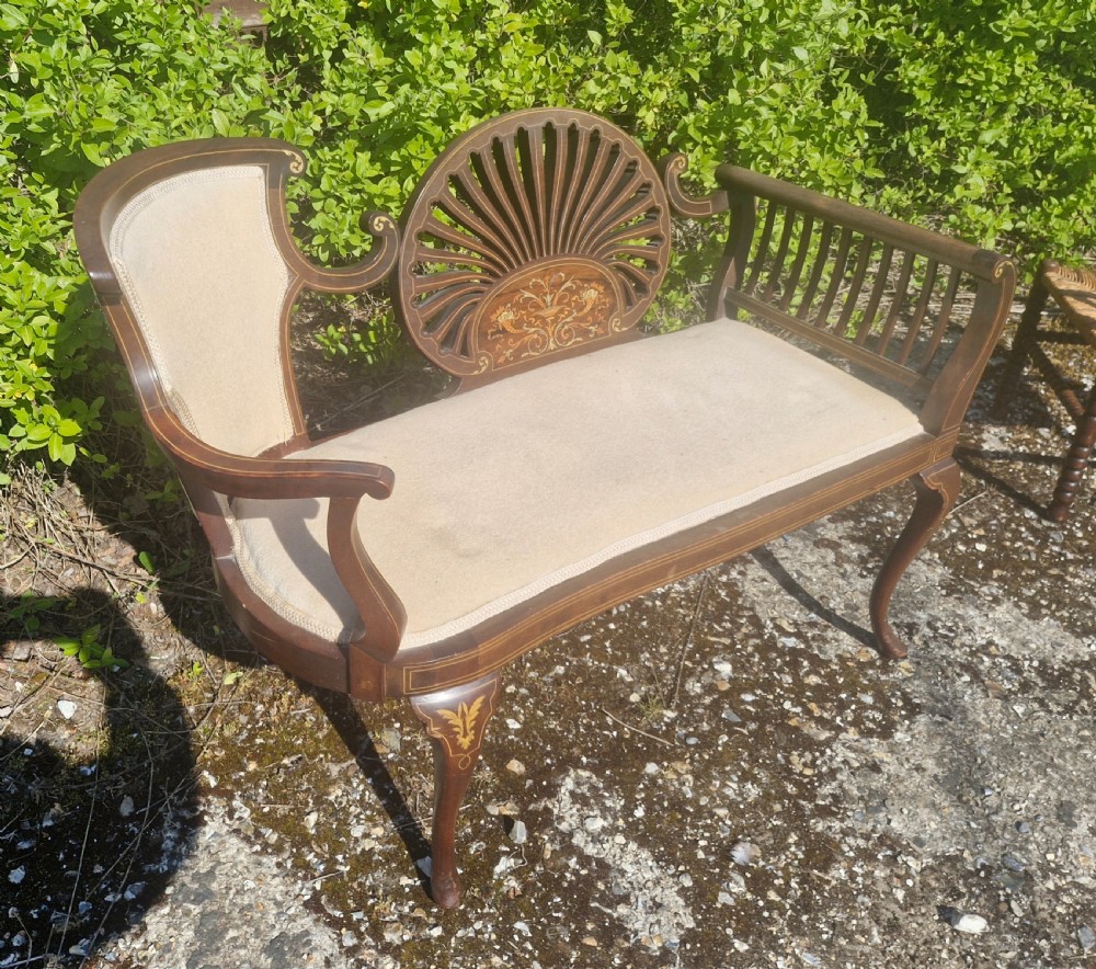 An Edwardian inlaid mahogany window seat with cream upholstery, a central carved fan splat, and scrolled arms. View IV