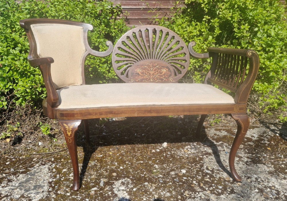 An Edwardian inlaid mahogany window seat with cream upholstery, a central carved fan splat, and scrolled arms. View V