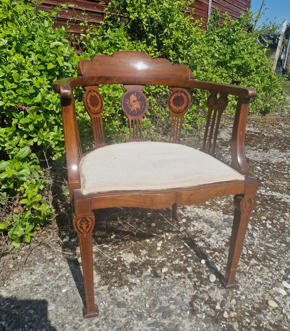 An Edwardian mahogany tub armchair featuring decorative marquetry inlay on the splats and front legs, curved armrests, and a light upholstered seat.