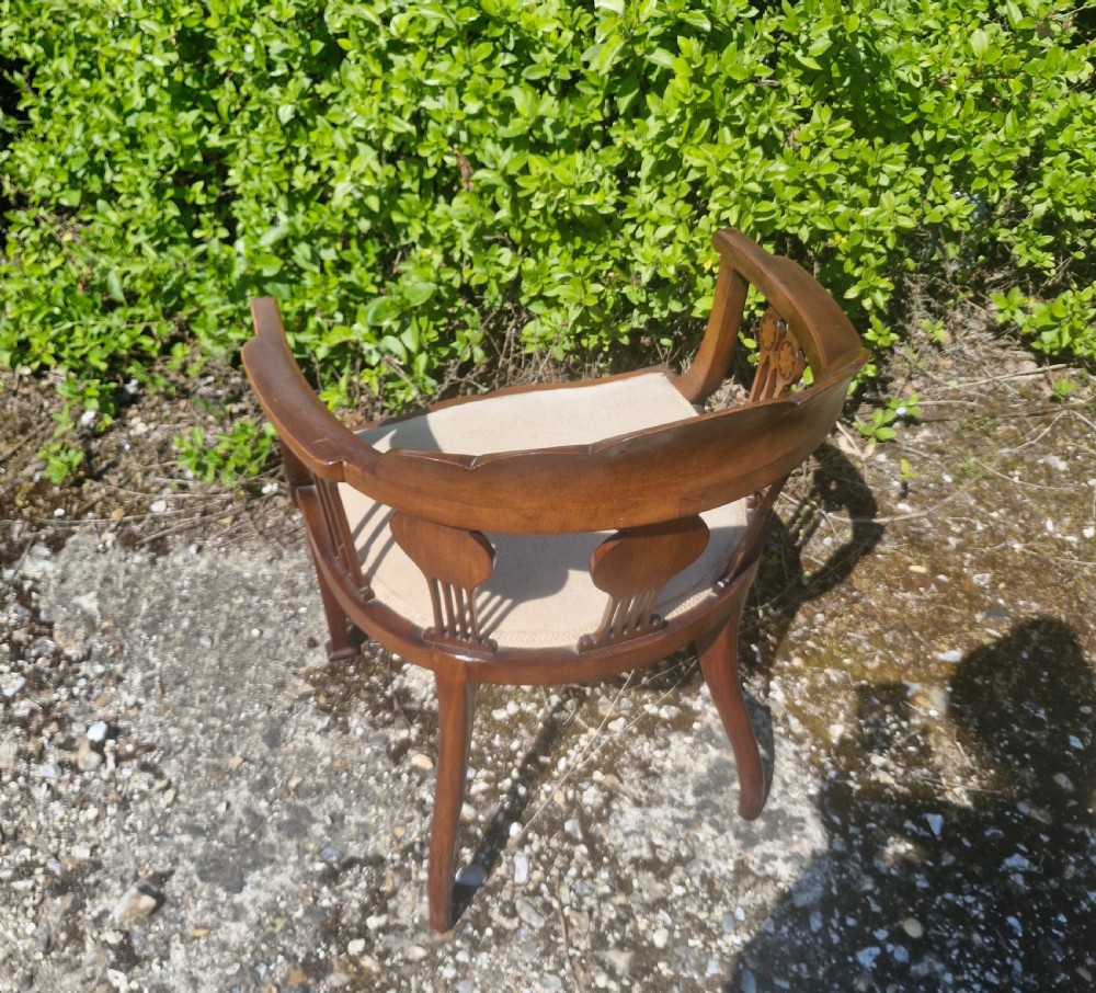 An Edwardian mahogany tub armchair featuring decorative marquetry inlay on the splats and front legs, curved armrests, and a light upholstered seat. View II