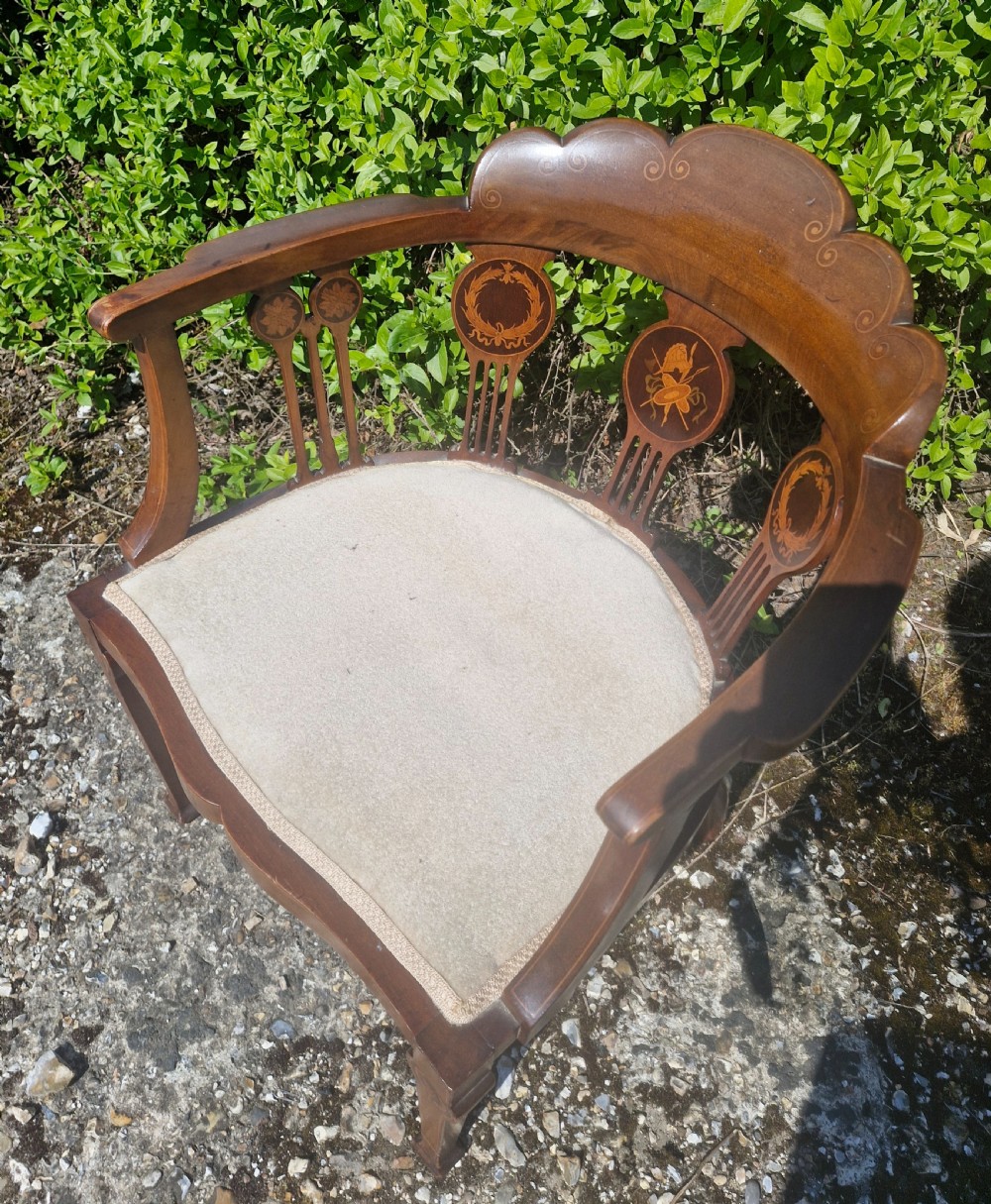 An Edwardian mahogany tub armchair featuring decorative marquetry inlay on the splats and front legs, curved armrests, and a light upholstered seat. View III