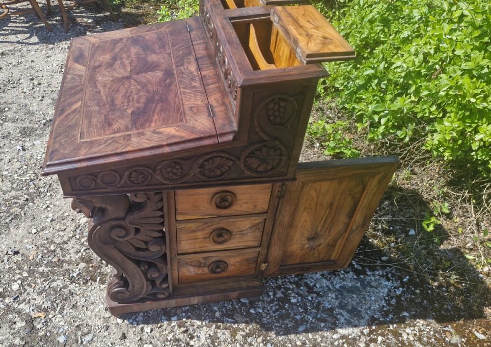 An antique carved olivewood Davenport writing desk with a sloped lid, foliage carvings, and decorative scrolled supports. View X