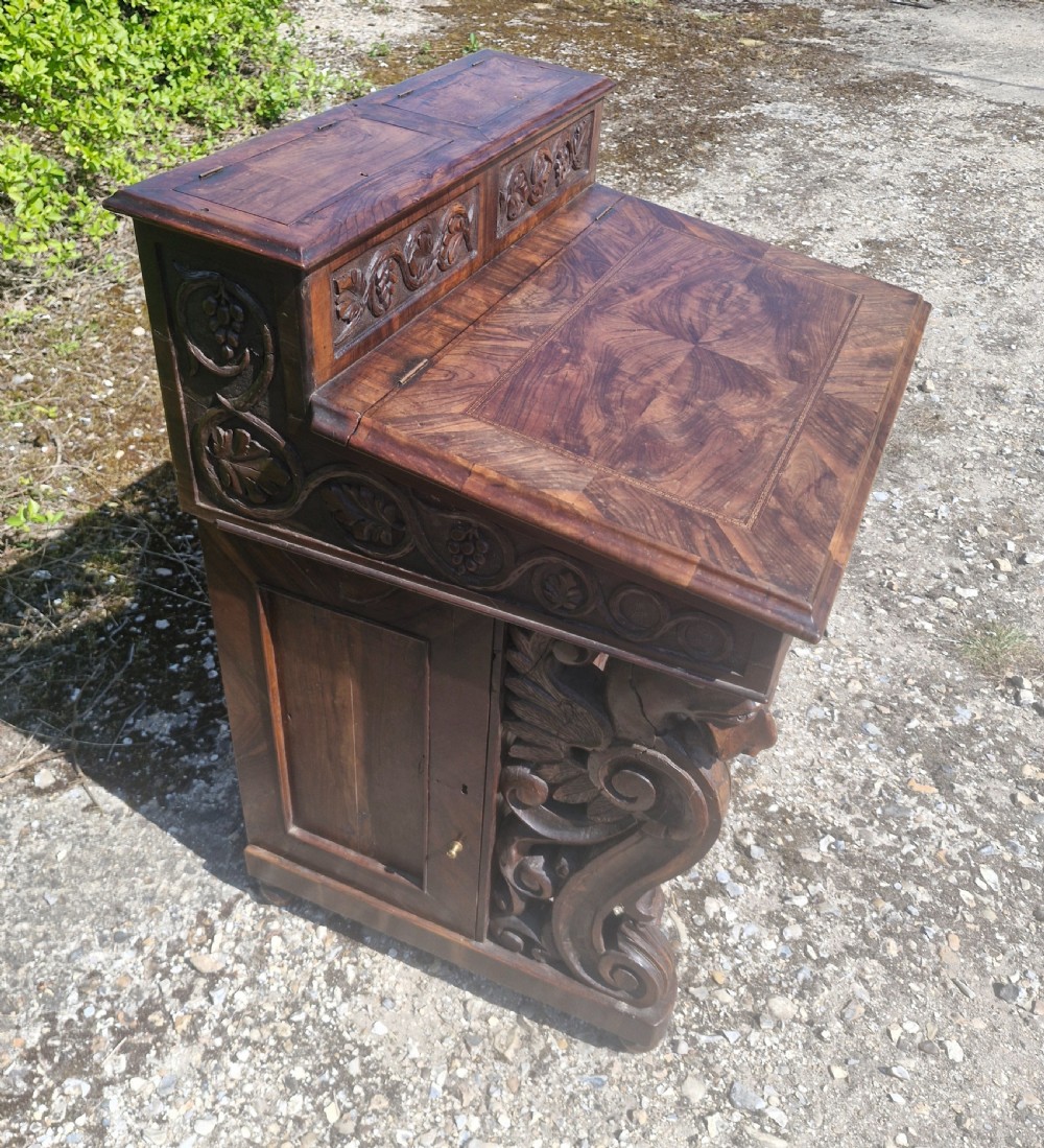 An antique carved olivewood Davenport writing desk with a sloped lid, foliage carvings, and decorative scrolled supports. View XIII