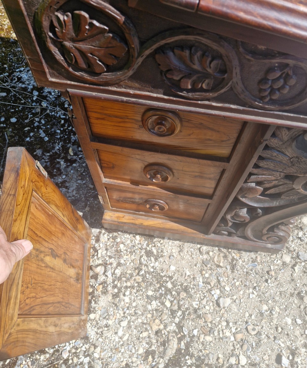 An antique carved olivewood Davenport writing desk with a sloped lid, foliage carvings, and decorative scrolled supports. View XIV