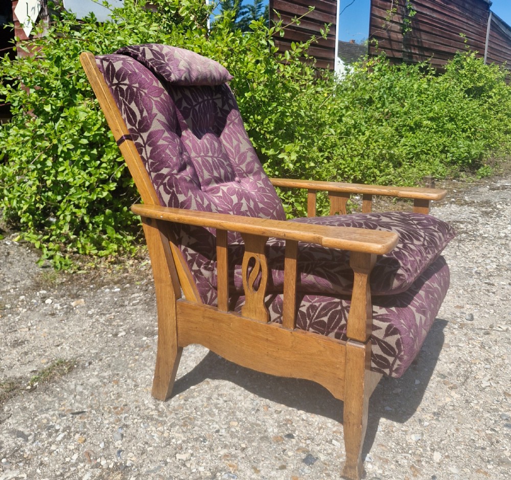 An Arts and Crafts oak reclining armchair with patterned purple upholstery and pierced side splats.