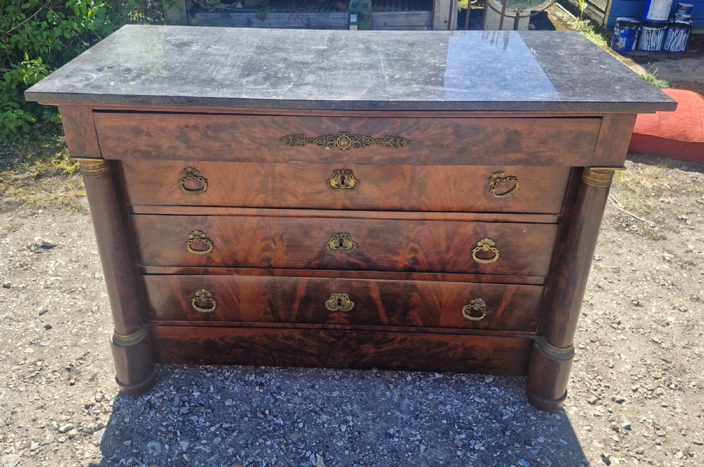 A nineteenth-century French mahogany chest of drawers featuring a dark grey marble top, four drawers with brass drop handles, and flanking side columns.