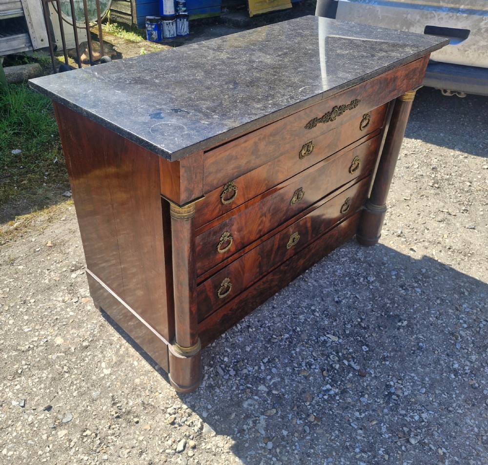 A nineteenth-century French mahogany chest of drawers featuring a dark grey marble top, four drawers with brass drop handles, and flanking side columns. View VII