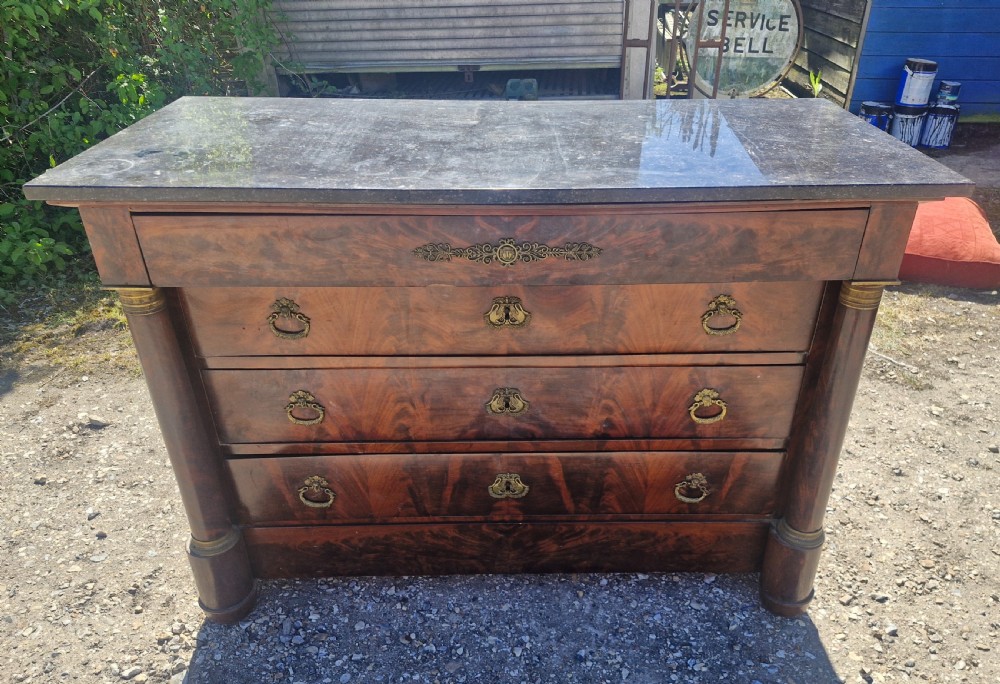 A nineteenth-century French mahogany chest of drawers featuring a dark grey marble top, four drawers with brass drop handles, and flanking side columns. View IX