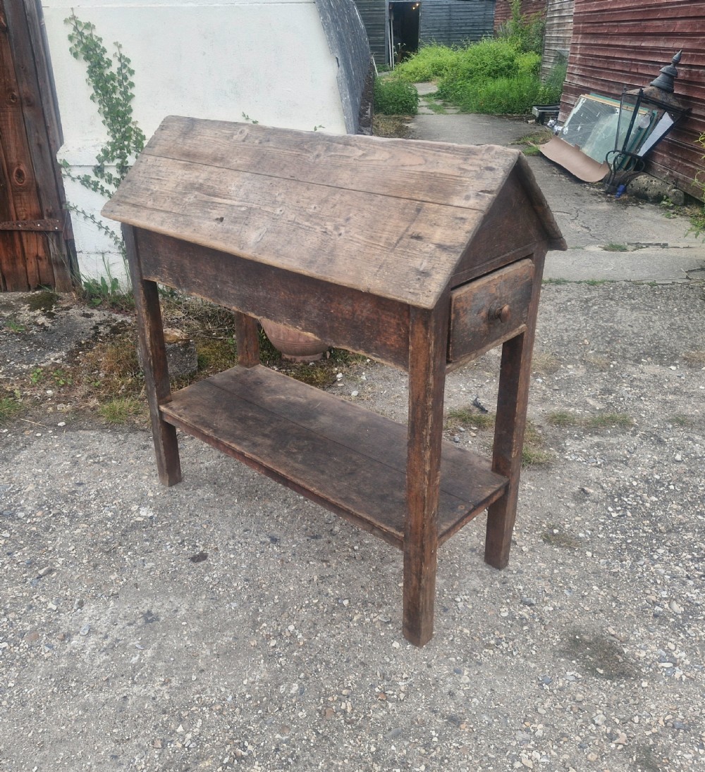 A freestanding Victorian weathered pine saddle rack featuring a pitched A-frame top, a single side drawer with a turned wooden knob, and a lower open shelf.