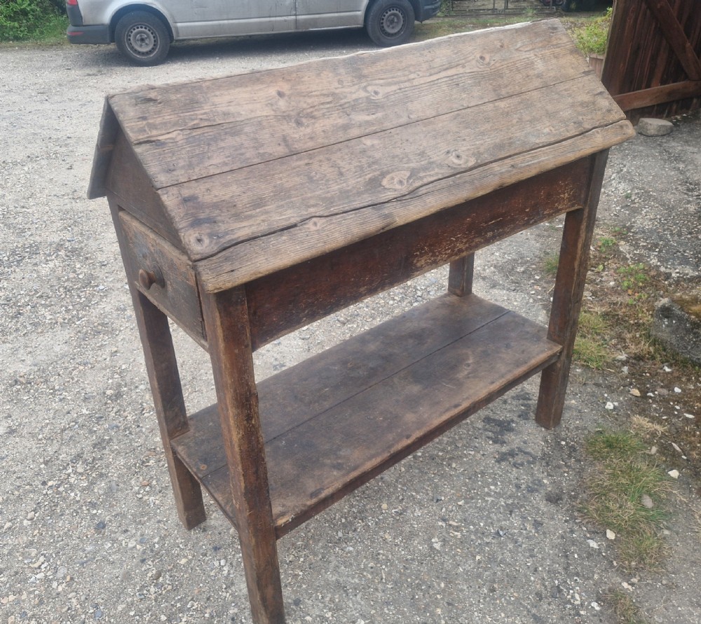 A freestanding Victorian weathered pine saddle rack featuring a pitched A-frame top, a single side drawer with a turned wooden knob, and a lower open shelf. View VI