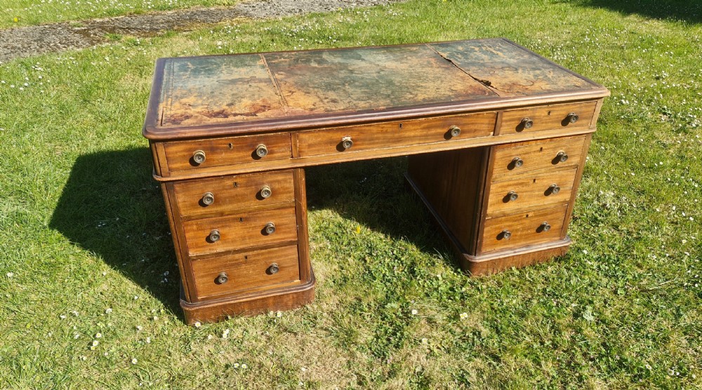A late Victorian mahogany kneehole desk featuring twin pedestals with drawers, a plinth base, and a worn leather writing surface.