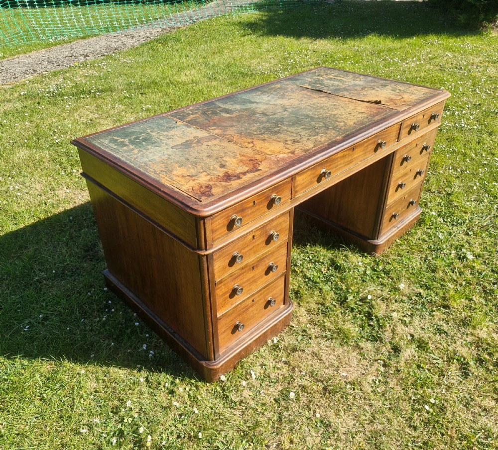 A late Victorian mahogany kneehole desk featuring twin pedestals with drawers, a plinth base, and a worn leather writing surface. View IV